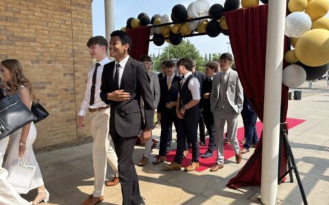 a group of students walking through a balloon arch, dressed in smart clothes, on their last day of year 11