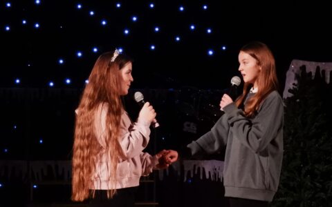 Two female students singing whilst holding hands