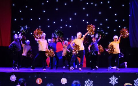 Primary school students dancing on stage with glittery pompoms